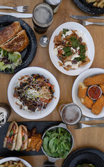 Food. Eating at the restaurant. Top view of variety of gourmet dishes, tableware and glasses of beer, on the wooden table. 