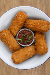 Gastronomy. Rustic presentation. Top view of fried mozzarella cheese fingers with a spicy dipping sauce, in a white bowl on the wooden table.