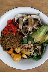 Vegan cuisine. Top view of a fresh salad, with sliced avocado, grilled pumpkin, quinoa, mushrooms, cherry tomatoes and roasted chestnuts, in a white bowl on the wooden table.