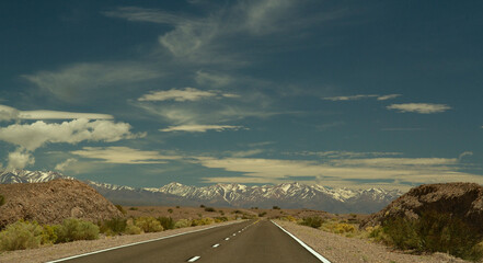 Traveling along the asphalt highway across the arid desert and into the Andes cordillera, under a beautiful blue sky with clouds. 