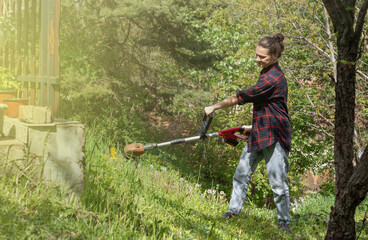 Woman in checkered shirt mowing grass with electric lawn mower.