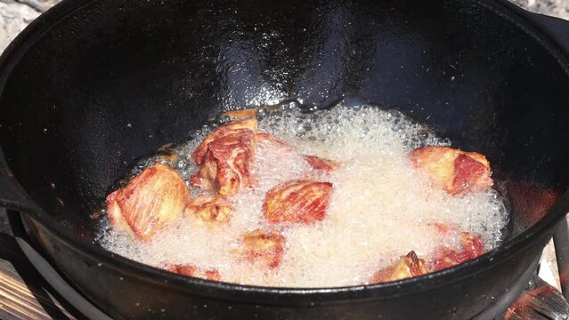 The meat is cut into pieces and boils in oil in a cast iron cauldron. The cook stirs the meat with a spatula. Cooking outdoors in national utensils. Roasted lamb and shinin.