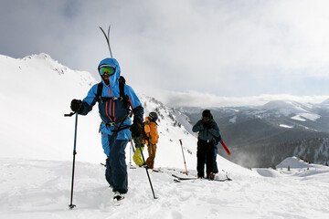 group of people climbing snowy hill on mountain on skis and splitboards