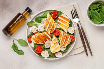 Vegetarian salad with spinach leaves, cherry tomatoes, mushrooms and grilled halumi cheese in a plate on the table. Top View