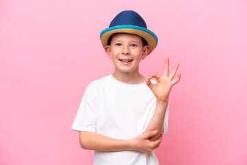 Little caucasian boy wearing a hat isolated on pink background showing ok sign with fingers
