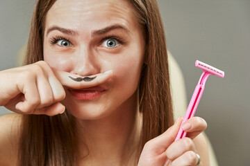 a pretty young woman holds a finger near her face, on which a funny mustache is drawn, and a pink...