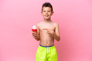 Little caucasian boy eating an ice-cream isolated on pink background and pointing it