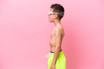Little caucasian boy wearing a diving goggles isolated on pink background laughing in lateral position © luismolinero