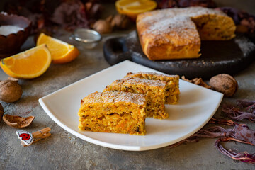 Delicious breakfast for the whole family: slices of pumpkin pie with oranges and walnuts on a wooden board on a gray background. Close-up.