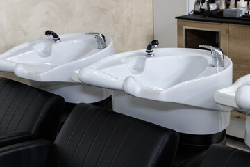 Professional black leather washing chairs with white wash sinks in hair salon interior.