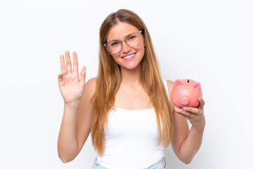 Young pretty blonde woman holding piggy bank isolated on white background saluting with hand with happy expression