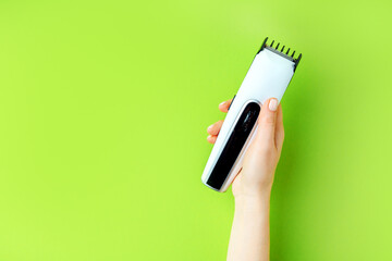 Female hand holding hair clipper on a green background with copy space.
