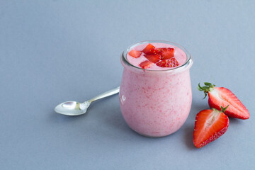 Natural milk yogurt with strawberry in the glass jar on the gray background. Closeup.