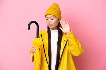 Young Chinese woman with rainproof coat and umbrella isolated on pink background making stop...