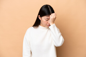 Young Chinese woman isolated on beige background with headache