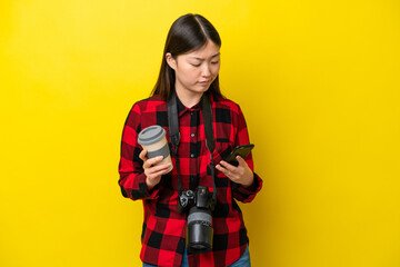 Young photographer Chinese woman isolated on yellow background holding coffee to take away and a...