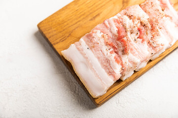 Board with pork fat, on a gray stone background. Salo. Delicious salty lard with pepper. Space for...