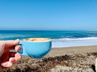 Blue cup of coffee on the beach