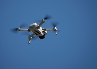 Drone with camera is flying high against a deep blue sky.