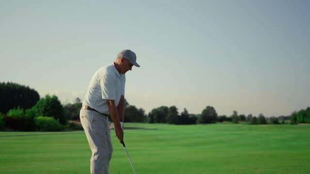 Senior golf player practicing hitting ball on grass field. Man training outdoors