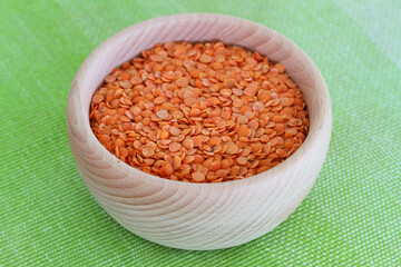 Uncooked red lentils in wooden bowl on green background

