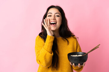 Young caucasian woman isolated on pink background shouting with mouth wide open while holding a bowl of noodles with chopsticks