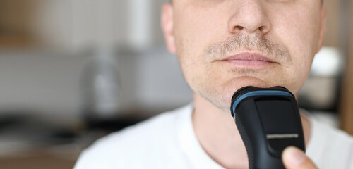 banner of close up of caucasian man in white t shirt is shaving beard with electric razor at bathroom at home. copy space. mans beauty concept. morning routine - Powered by Adobe