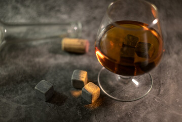 transparent whiskey with a bottle and a wooden cork on a dark background. whiskey stones in a glass