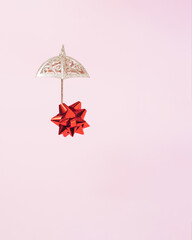 Falling red present bow on umbrella on bright pink background. Waiting for present. Minimal gift concept with copy space for greeting card or message. Grab a gift or sale, falling prices.