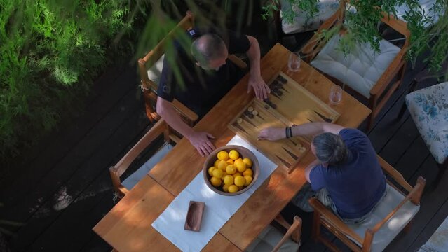 Two man playing backgammon on patio under trees