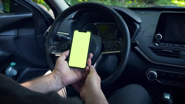 Man inside modern car holding phone with frameless design and blank green screen. close-up