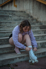 Teenage girl is tying the laces of roller skates before practicing. She is sitting on stairs.