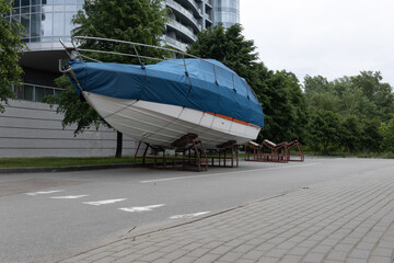 A motor boat covered with a blue cover stands on land under the open sky against the background of...