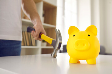 Cute yellow ceramic piggy bank about to be smashed with a hammer. Man in dire need of money is going to break his piggybank on the table. Cropped close up shot. Saving up, or being in debt concepts
