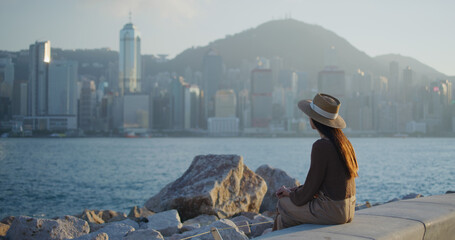 Woman sit beside the sea and look at the city of Hong Kong