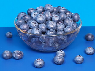 Fresh, ripe blueberries in a glass container. Blueberries on a blue background. Healthy dessert