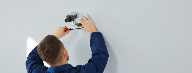 Back view of man using screwdriver while setting up new modern wall mounted security camera. Young...