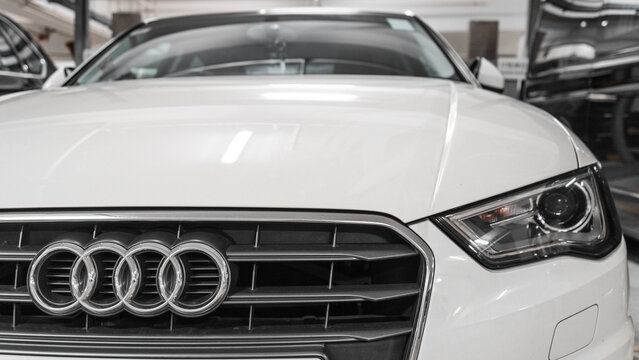 Close-up of Audi logo badge, headlights and car grill on a white Audi S3 hatchback sportback car.