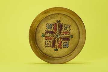 An old wooden plate with colorful decorations. Isolated on a yellow background.