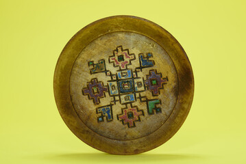 An old wooden plate with colorful decorations. Isolated on a yellow background.