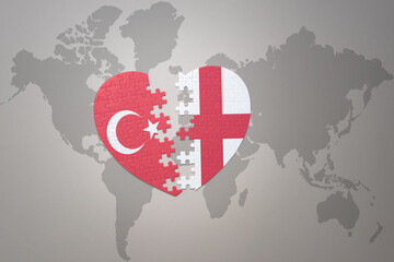 puzzle heart with the national flag of turkey and england on a world map background. Concept.