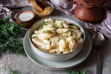 Family lunch: German dumplings with potatoes and onions in a beautiful plate on a gray background. Close-up