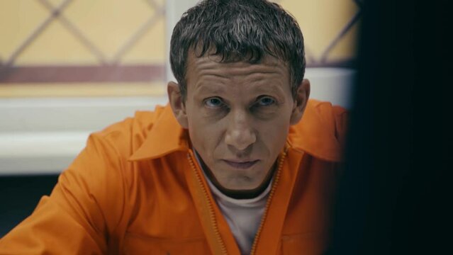 The prisoner in the orange robe sits at the table.