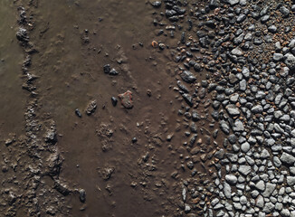 Pebbles, round stones in a muddy puddle, top view. Texture of wet earth and stone.