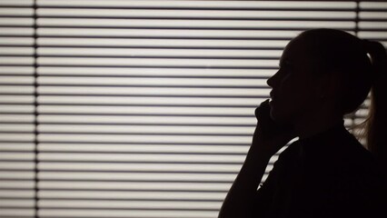 Shadow of woman talking on phone close-up, silhouette of female person calling on smartphone on white striped background. - Powered by Adobe
