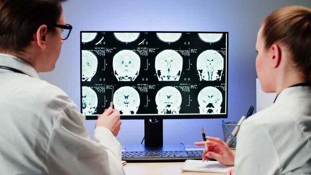 Doctors examining X-ray on computer monitor. Magnetic resonance image of head. Man and woman nurse looking at human brain MRI close-up. Advanced research of body, checkup tomography. 