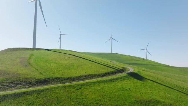 Windmill park green energy from drone view, windmill wind farm on green hills with rotating windmill turbine blades generating renewable energy from wind. 4k cinematic aerial California countryside