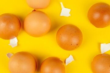Many brown broken eggshells on yellow background top view
