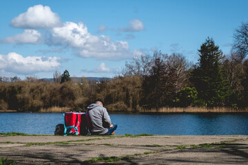 Lonely food delivery man with his typical cubic backpack sitting on the bank of the river Calle-calle on a sunny day with blue sky, Valdivia, Chile (in black and white)