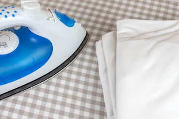 Ironing at home with an electric iron and a pile of folded white clothes on ironing board